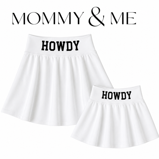 Two white pleated skirts with black 'HOWDY' text on the waistbands, shown on a white background with 'MOMMY & ME' text above. One skirt is larger and one is smaller, suggesting a matching set.
