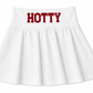A white pleated skirt with the word 'HOTTY' printed in bold red block letters across the waistband, shown against a plain white background. Made for gameday. It is a Mississippi skirt. 
