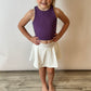 Girl wearing a white athletic skirt with the words geaux on it. She pairs it with a purple athletic top and matching bow. 